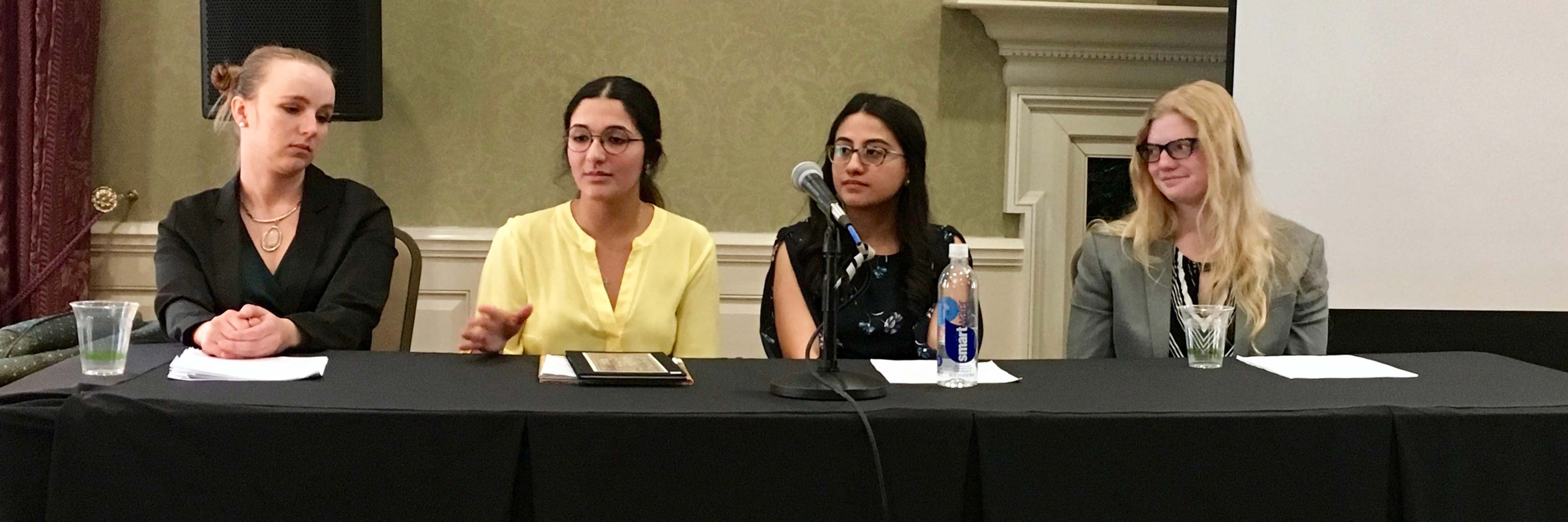 Four female students in business dress sitting at a panel presentation.